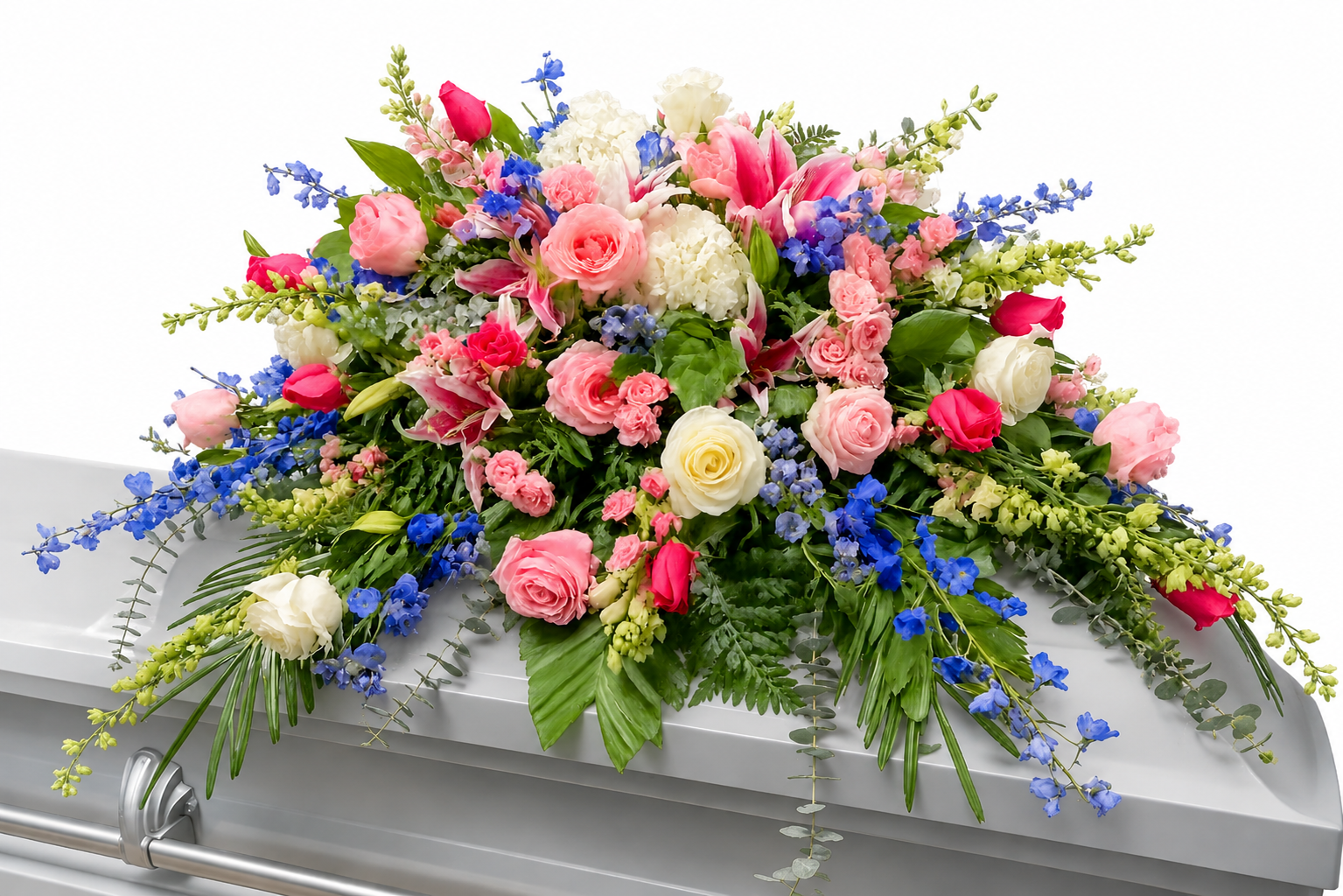 A casket spray featuring pink roses, blue delphinium, white hydrangea, and mixed greenery arranged in a full design across a white casket, displayed against a clean white background.