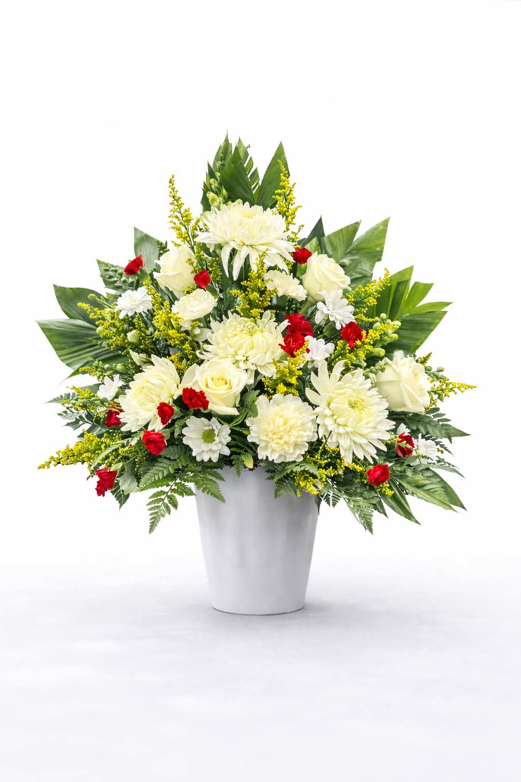 Elegant sympathy flower arrangement featuring white chrysanthemums, roses, yellow solidago, red mini carnations and greenery in a white plastic container. All white background.