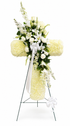 Elegant heart-shaped sympathy wreath made of artificial candlestick white carnations, accented with artificial white lilies, artificial white roses, artificial lush greenery, and a flowing white ribbon, displayed on a white easel against a clean neutral background.