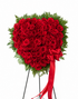 Heart-shaped standing sympathy wreath made entirely of deep red roses, framed with lush green foliage and accented with flowing red ribbon bows, displayed on a green easel against a white background.