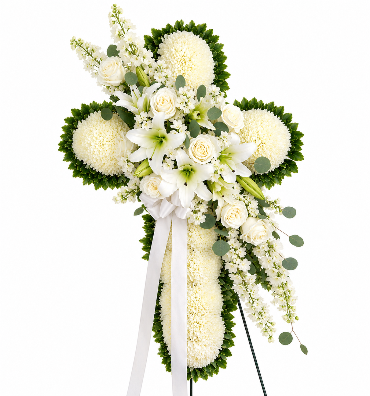 A white and green cross-shaped floral arrangement on a stand, featuring white roses, lilies,  mums, eucalyptus leaves, and long white ribbons, photographed on a plain white background.