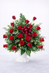 Red rose sympathy flower arrangement with fillers and greenery in a white pedestal urn. White background