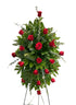 Elegant standing sympathy spray featuring deep red roses nestled among rich green foliage and cascading greenery, arranged in a classic vertical design on a green easel against a white background.