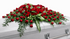 Classic red rose casket spray featuring over 100 of deep red roses accented with baby’s breath and lush greenery, arranged in a full, cascading design atop a white casket in a softly lit chapel setting.