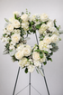 Elegant white sympathy open heart wreath featuring ivory roses, white hydrangea, soft textured greenery, and subtle berry accents, arranged in a classic heart design on a green easel against a neutral background.