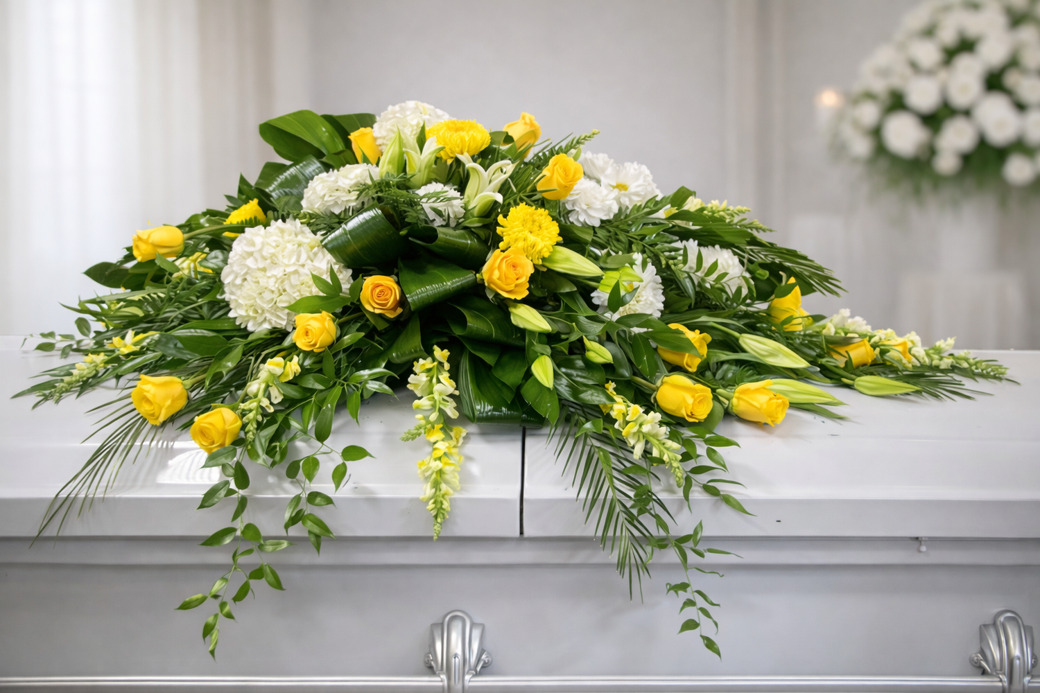 Bright casket spray featuring yellow roses, white hydrangea, white lilies, and cascading greenery, arranged in a full, elegant design atop a white casket in a softly lit chapel setting.