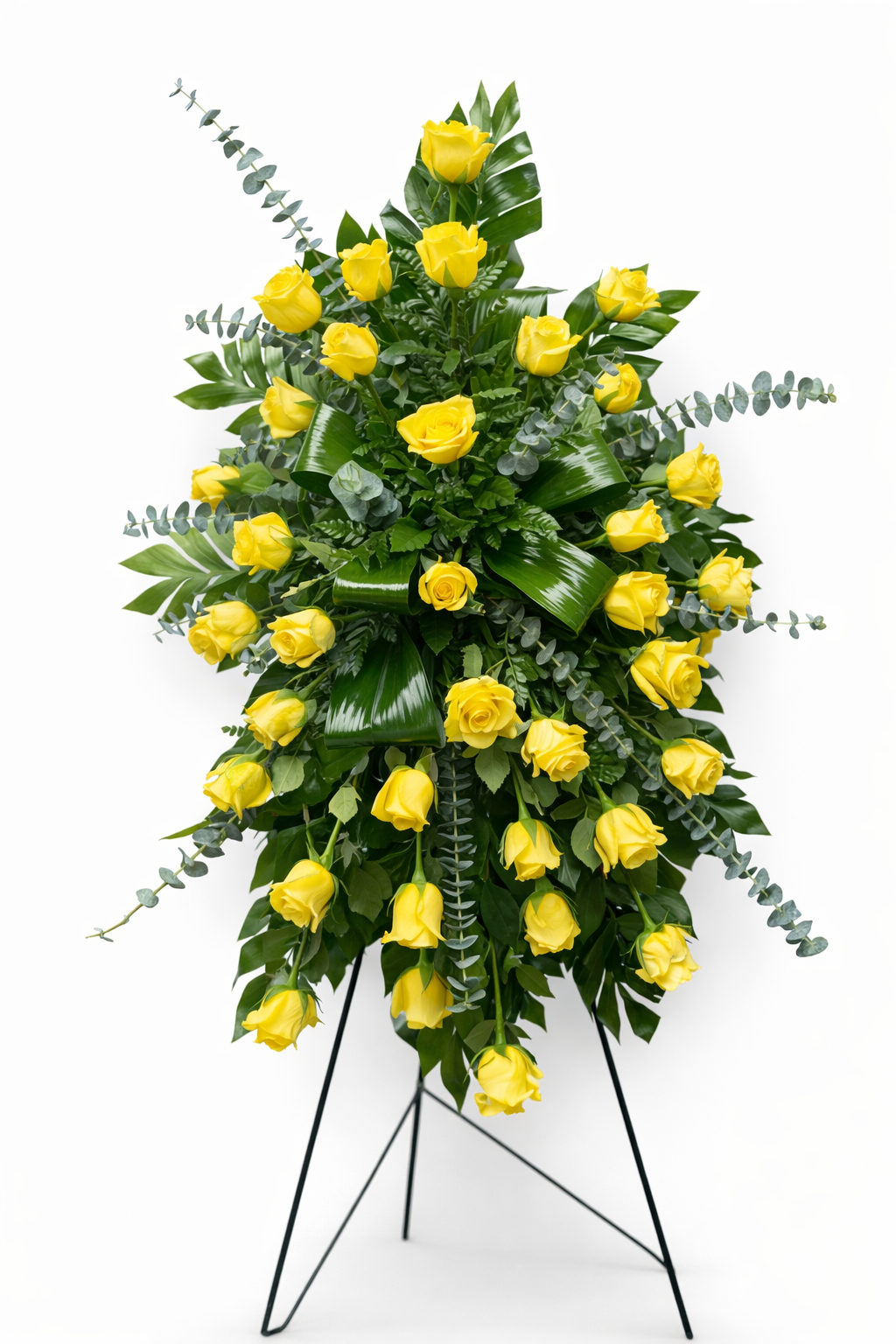 Bright standing sympathy spray featuring vibrant yellow roses accented with lush tropical greenery and eucalyptus, arranged in a bold, cascading design on a green easel against a clean white background.