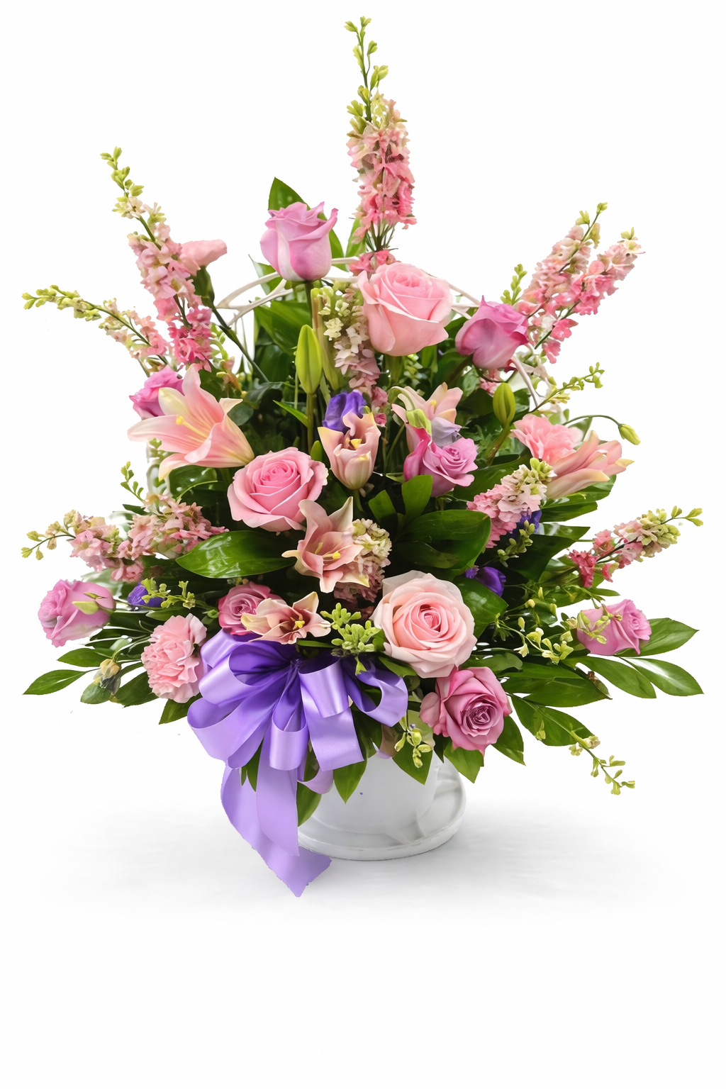 A pastel sympathy flower basket featuring pink roses, blush lilies, snapdragons, and soft seasonal flowers arranged in a white handled basket with a lavender ribbon, displayed against a clean white background.