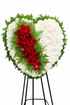 Heart-shaped sympathy wreath featuring white carnations accented with a cascading ribbon of deep red roses and lush greenery, arranged in a bold, elegant design on a green easel against a clean white background.