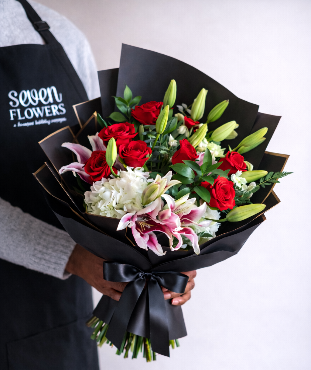 Elegance in Bloom Bouquet featuring red roses, pink lilies, white hydrangea, and greenery wrapped in luxury black floral paper with a satin bow, arranged in an elegant hand-tied design.