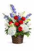 Elegant sympathy basket arrangement featuring red roses, soft blue hydrangea, blue delphinium, white snapdragons, and delicate white accent flowers, complemented by lush green foliage and arranged in a woven basket against a clean white background.