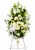 Classic white standing sympathy spray featuring white lilies, white roses, white cremon mums, carnations, delicate filler flowers, and lush palm and fern greenery, arranged in a full, cascading design on a green easel against a soft neutral background.